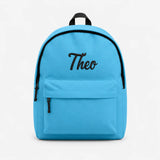 A bright blue backpack with black trim, a top handle, a front zippered pocket, and the name 'Theo' embroidered in black script on the front, shown against a plain white background.